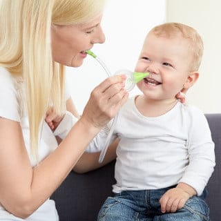 Eine Frau reinigt die Nase ihres lächelnden Sohnes mit Hilfe des Nosiboo Eco manuellen Baby Nasensaugers