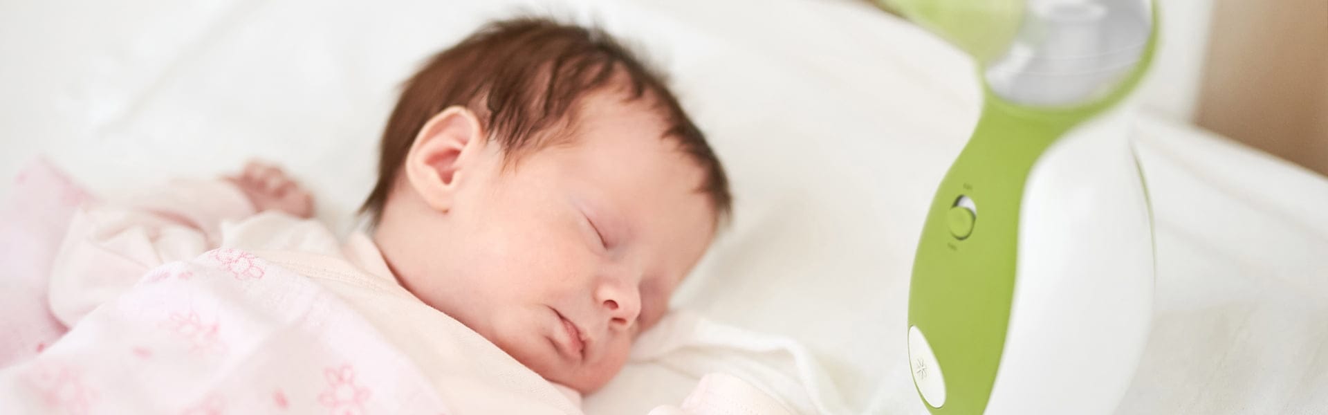 Ein Baby schläft friedlich im Babybett neben dem tragbaren Baby Nasensauger Nosiboo Go