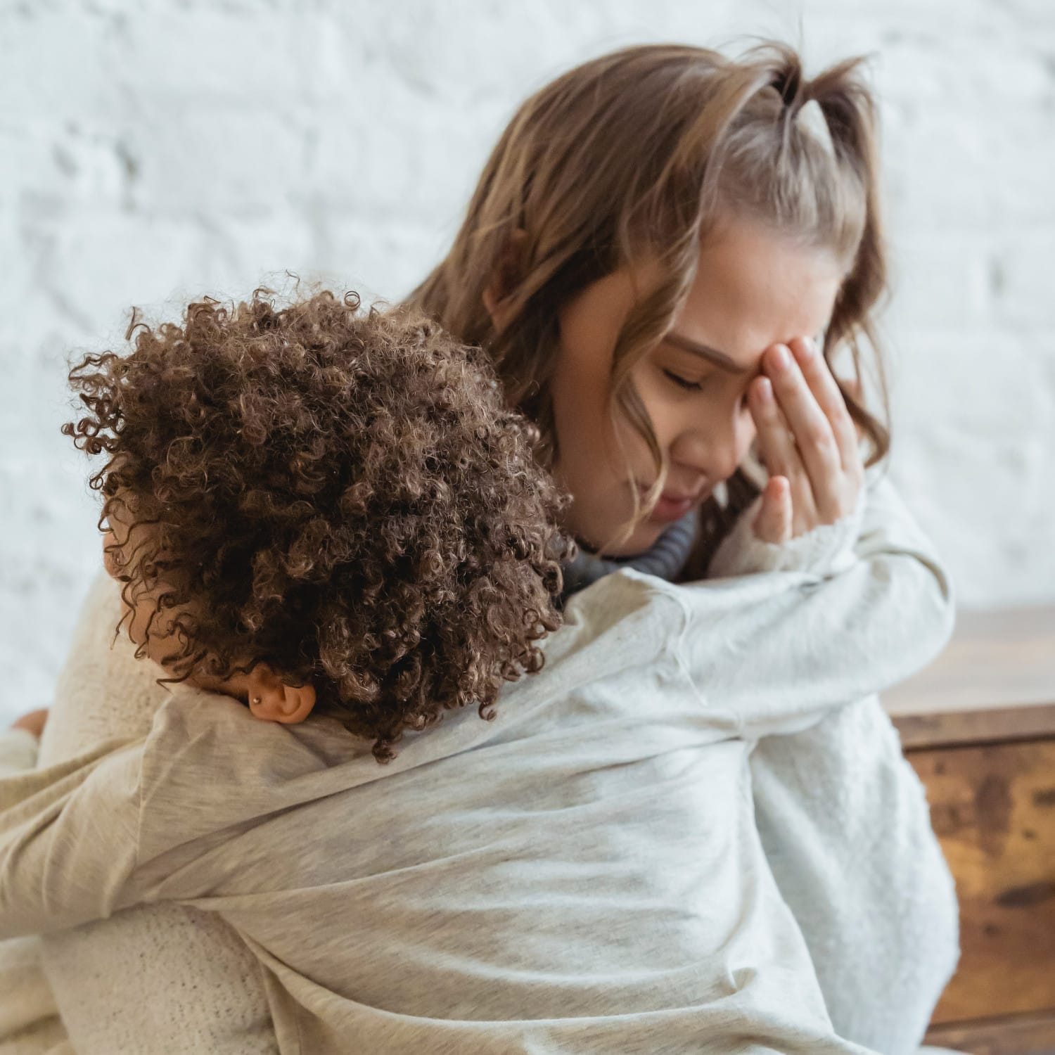 Eine besorgte Frau fängt ihren Kopf, während sie ihr Kind umarmt.